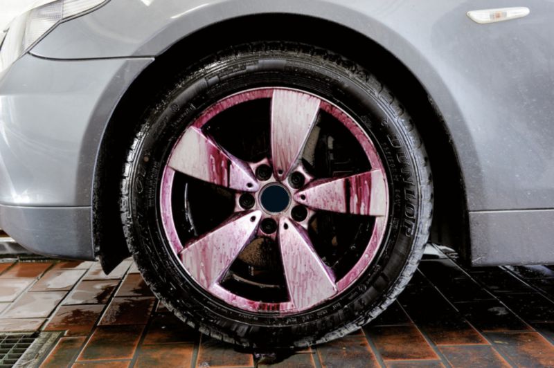 Proceso de limpieza de las ruedas del coche. El limpiador de llantas  produce una reacción química púrpura al eliminar las inclusiones de metal o  hierro y el polvo de los frenos. Detalle